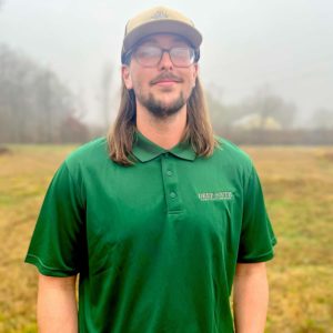Photo Austin Hood, Senior Technician for Deep South Construction Pros standing in a field wearing a green branded T-shirt.