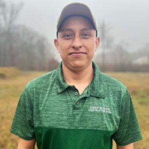 Photo Estuardo, Crew Member for Deep South Construction Pros standing in a field wearing a green branded T-shirt.